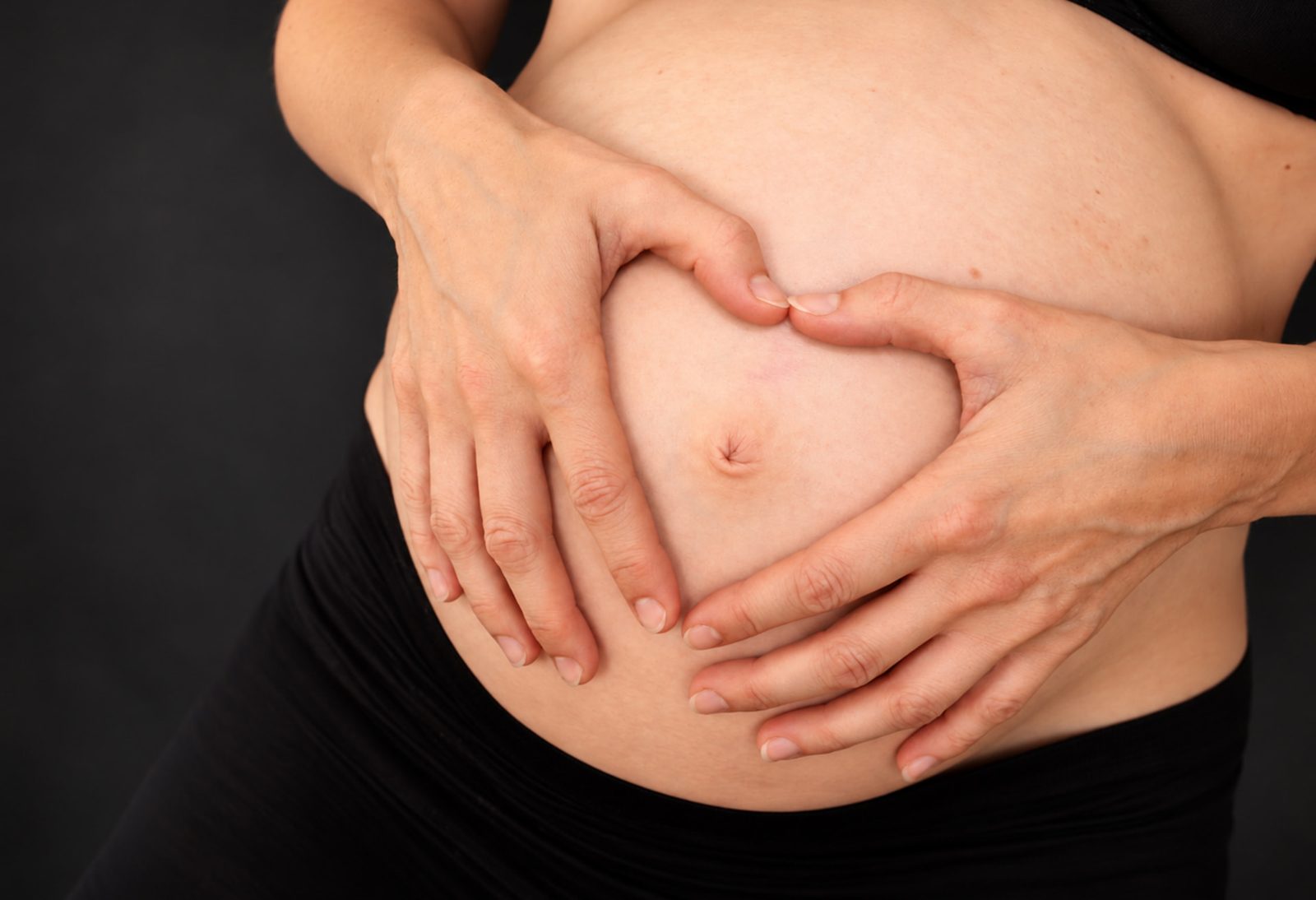 Hände formen ein Herz auf dem Babybauch